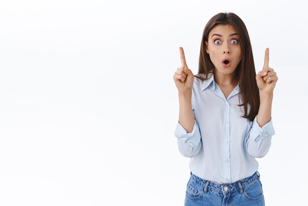 Incredible best offer hurry up click it Astounded and amazed speechless young woman pointing fingers up make surprised shocked face at camera open mouth wondered white background