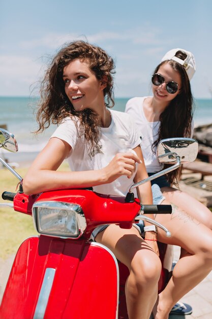 Incredible two happy woman have fun and traveling by red motorbike in sunshine on the island by the ocean and nature, true happy emotions, travel, trip, happy emotions