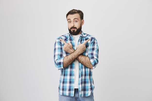 Indecisive adult bearded male customer pointing sideways