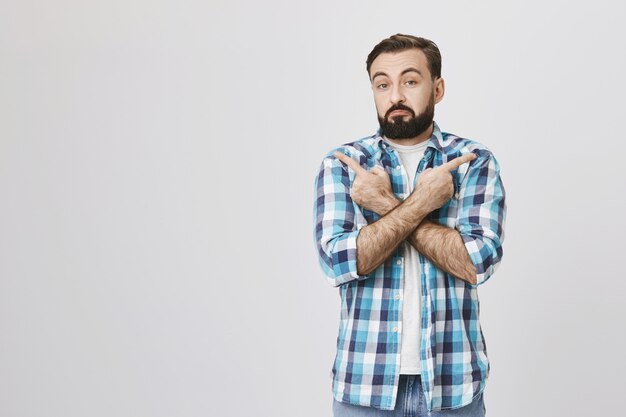 Indecisive adult bearded male customer pointing sideways