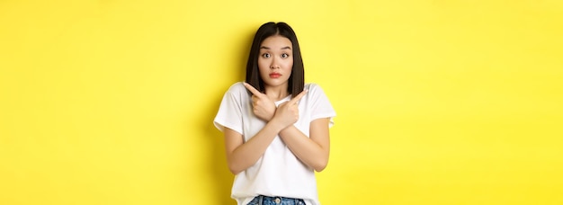 Indecisive asian girl need help with choice pointing fingers sideways and looking confused standing