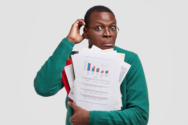 Нерешительный темнокожий мужчина чешет затылок, несет бумаги с данными и диаграммой