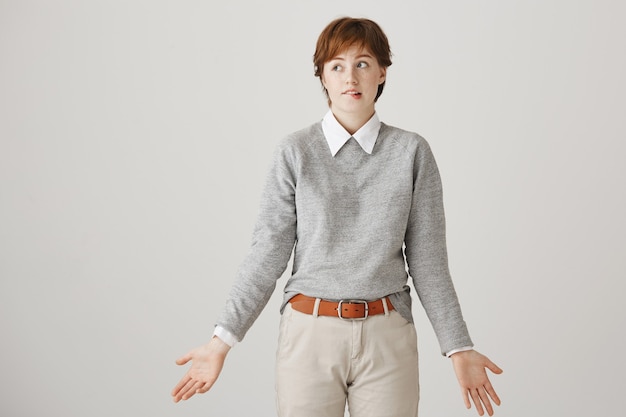 Free photo indecisive clueless redhead girl with short haircut posing against the white wall