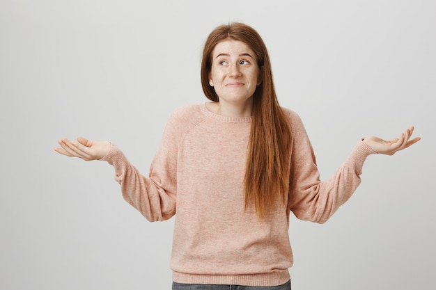 Indecisive cute redhead female shrugging unaware, look away and smiling