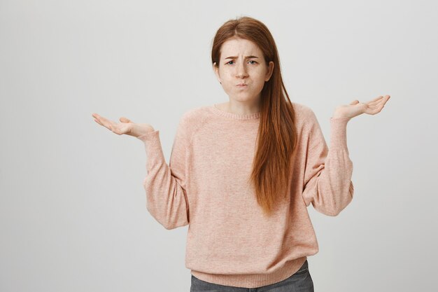 Indecisive cute redhead girl shrugging, standing clueless