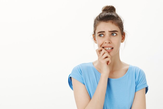 Indecisive and puzzled young woman biting fingernail and looking away troubled, feeling worried and confused