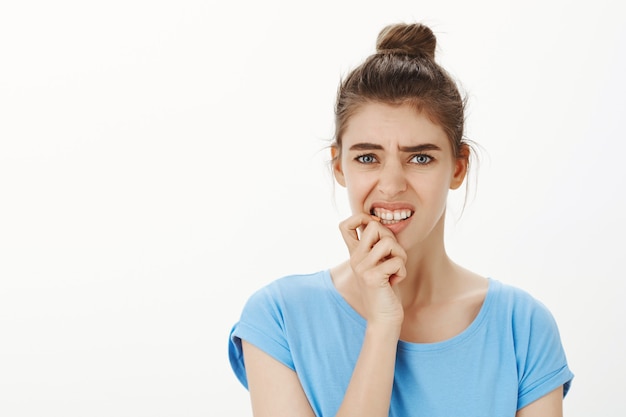 Foto gratuita giovane donna indecisa e perplessa che si morde un'unghia e sembra turbata, si sente preoccupata e confusa