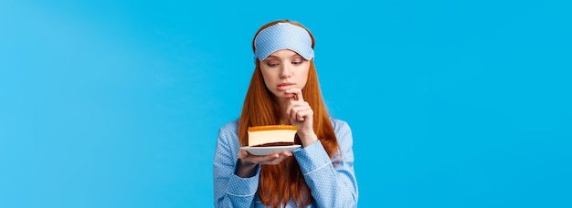 Indecisive redhead girl cant resist temptation biting finger and looking with desire at slice cake w