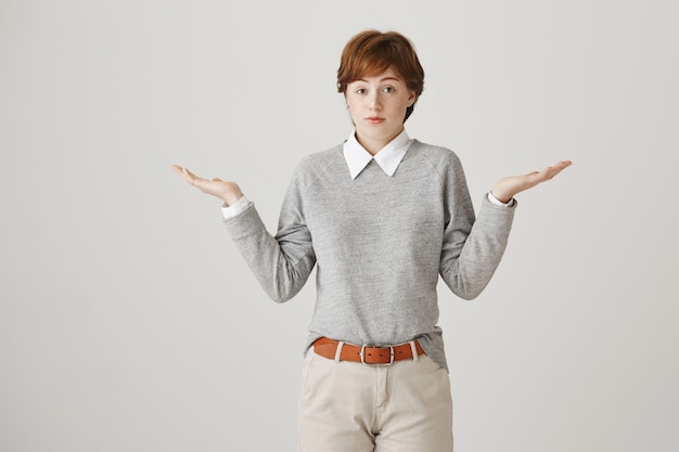 Free photo indecisive redhead girl with short haircut posing against the white wall