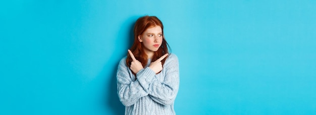 Free photo indecisive redhead teenage girl making decision pointing fingers sideways and looking left doubtful