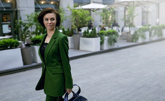 Independent lady walking down the street, holding her purse. Fashionable green jacket on her. Short and sexy haircut, confident and smart