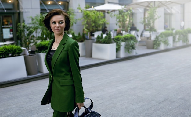 彼女の財布を持って通りを歩いている独立した女性。彼女のファッショナブルな緑のジャケット。短くてセクシーなヘアカット、自信を持ってスマート