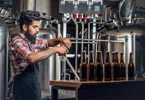 Free photo indian bearded tattooed hipster male manufacturer presenting craft beer in the microbrewery.