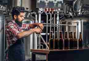 Free photo indian bearded tattooed hipster male manufacturer presenting craft beer in the microbrewery.