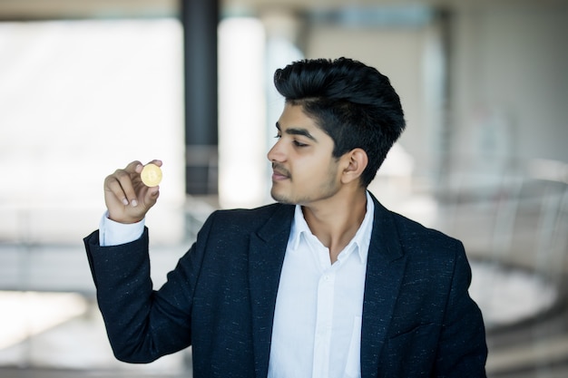Indian business man in suit with golden bitcoin in modern office