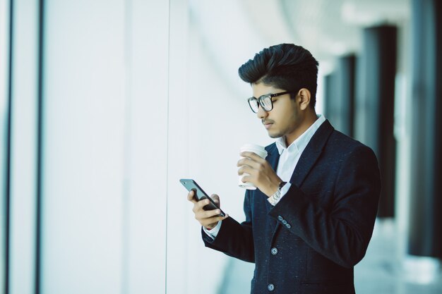 Indian businessman uses phone and drink coffee in office