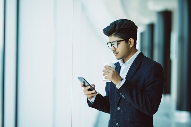 Индийский бизнесмен использует телефон и пьет кофе в офисе