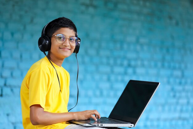 노트북과 헤드폰을 사용하는 인도 아이. 온라인 수업 참석