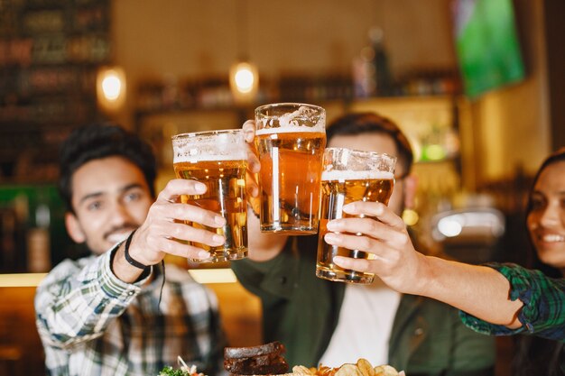 Indian friends in a pub. Guys and girl at  bar. Celebration over a mug of beer.