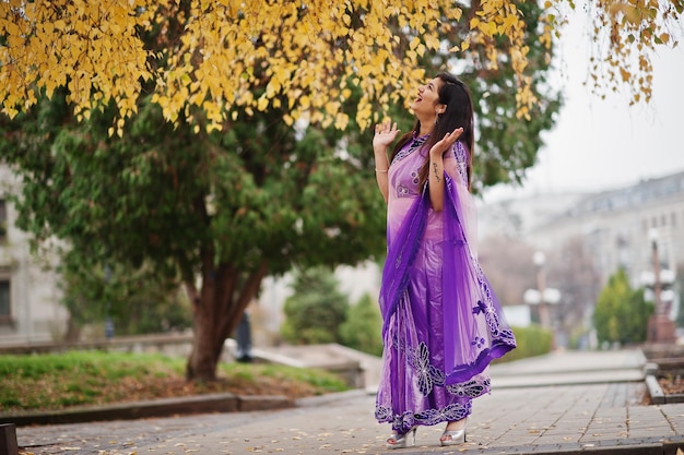 가을 거리에서 포즈를 취한 전통적인 보라색 사리에 인도 힌두교 소녀