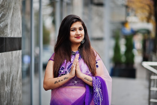 Индийская индуистская девушка в традиционном фиолетовом сари позирует на улице и показывает намасте татуированные руки знак