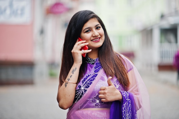 Free photo indian hindu girl at traditional violet saree posed at street and speaking on phone shows thumb up