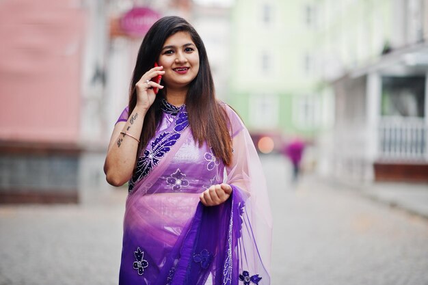 Индийская индуистская девушка в традиционном фиолетовом сари позирует на улице и разговаривает по телефону