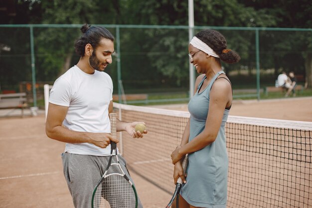 Indian man and black american woman standing on a tennis court.