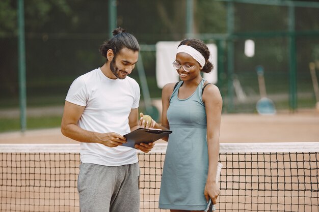 Indian man and black american woman standing on a tennis court.