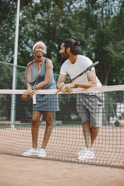 Индийский мужчина и темнокожая американка, стоящие на теннисном корте
