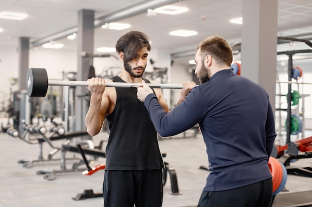 Indian man doing excercisses on special equipment at gym with personal trainer