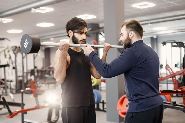 Индийский мужчина делает упражнения на специальном оборудовании в тренажерном зале с личным тренером