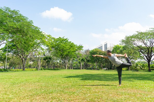 Indian man doing lord of dance pose outdoors in summer city park with trees 