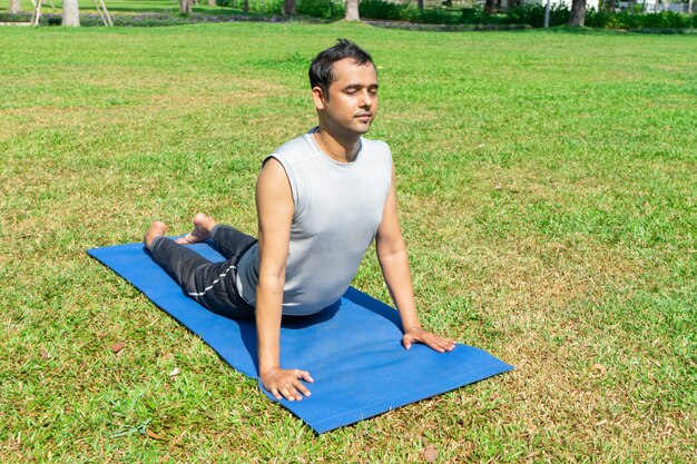 Indian man doing upward facing dog pose outdoors on green lawn. Outdoor yoga concept
