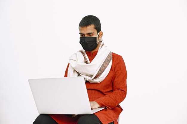 Indian man in national costume working with laptop on a white wall.