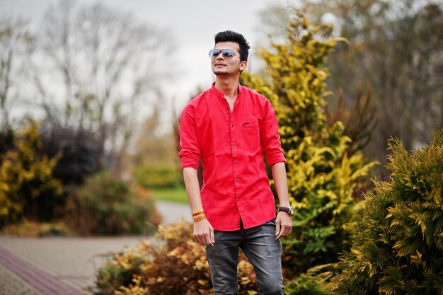 Indian man at red shirt and sunglasses posed outdoor