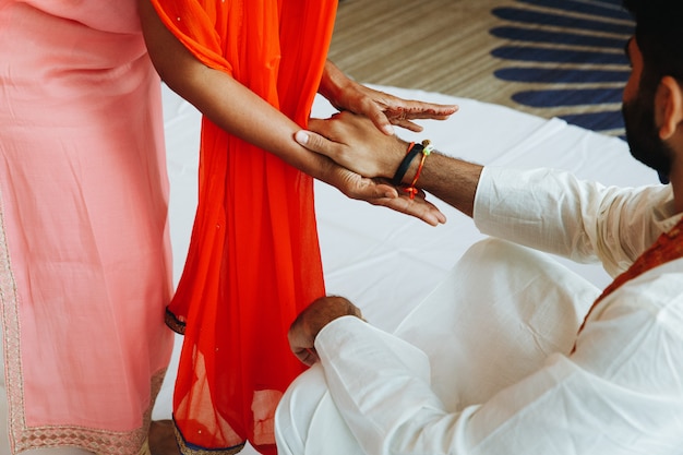 Индийский мужчина в белой одежде и женщина в лососевом платье держатся за руки