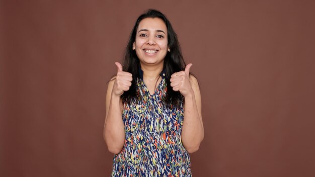 Indian model showing okay sign and thumbs up gesture in studio, giving like and agreeing with optimistic idea. Friendly positive approval ok symbol to accept excellent agreement.