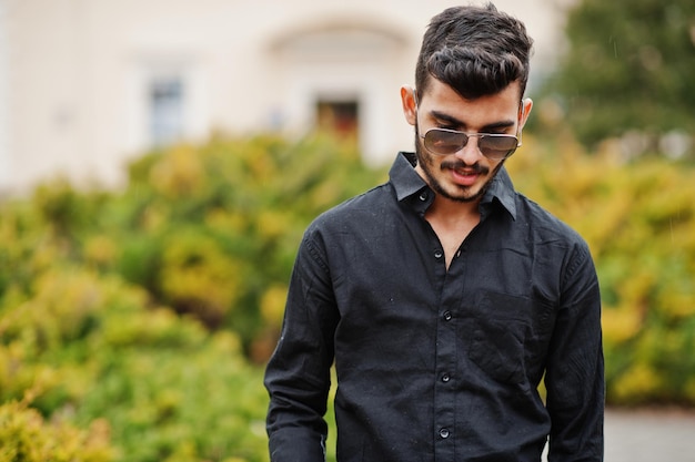 L'uomo alla moda indiano alla camicia e agli occhiali da sole neri ha posato all'aperto
