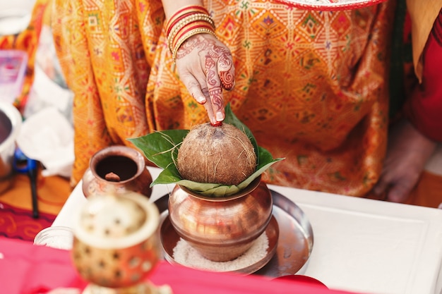 Indian woman holds a coconut over the mango leaves put in bronze