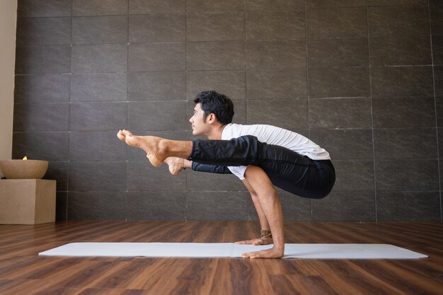 Indian yogi doing firefly yoga pose in gym