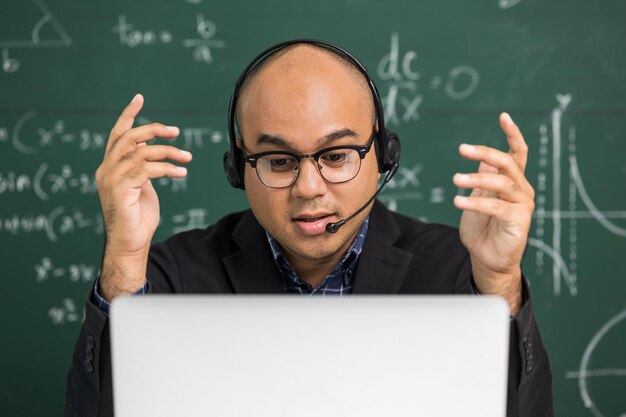 Indian young teacher man sitting wearing headset teaching online video conference by laptop Premium Photo