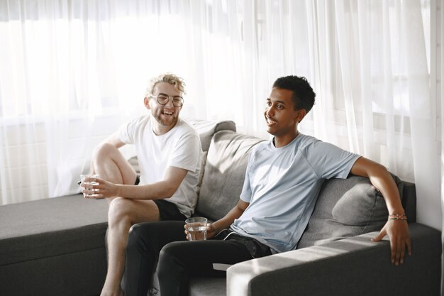 Indiand and European men watching film. They are sitting on a couch.