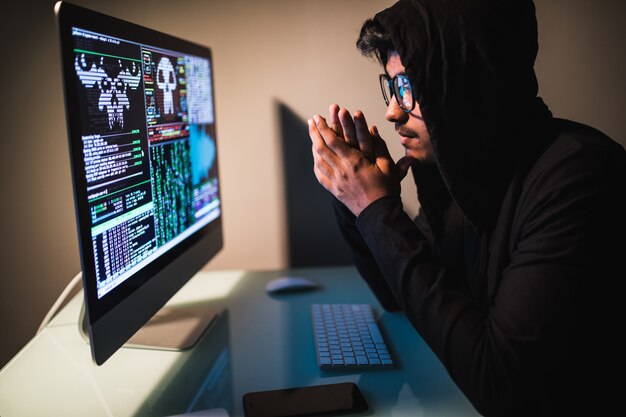 Indianmale hacker with smartphone and coding on computers screen in dark room