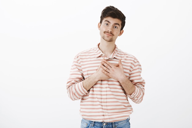 Indifferent sarcastic european man with moustache, smirking and holding palms over heart, imitating pleasure and thankful attitude, standing