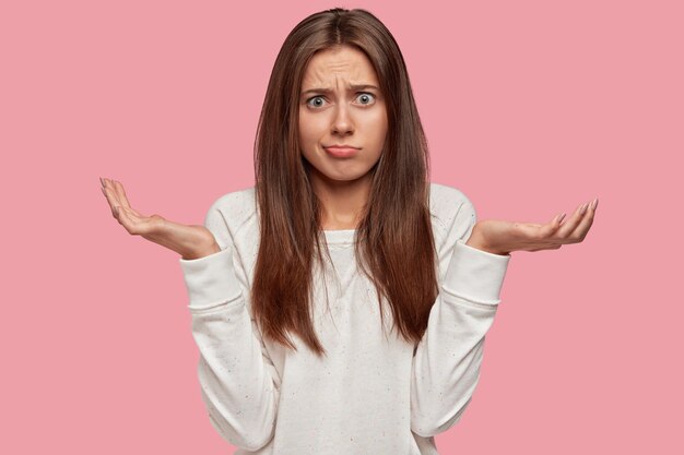 Indignant beautiful brunette posing against the pink wall