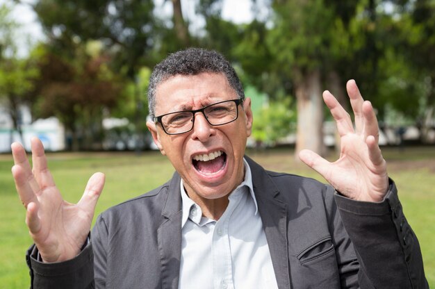 Indignant middle-aged man screaming and raising hands in park