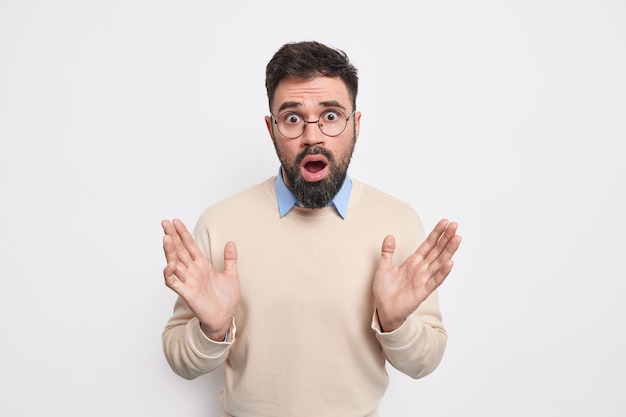 Indignant puzzled bearded adult man raises palms looks confused, has surprised face expression cannot believe in something unexpected wears casual jumper 