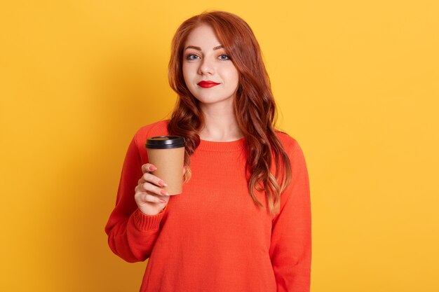 Indignant woman with calm facial expression, has coffee break, holds paper cup