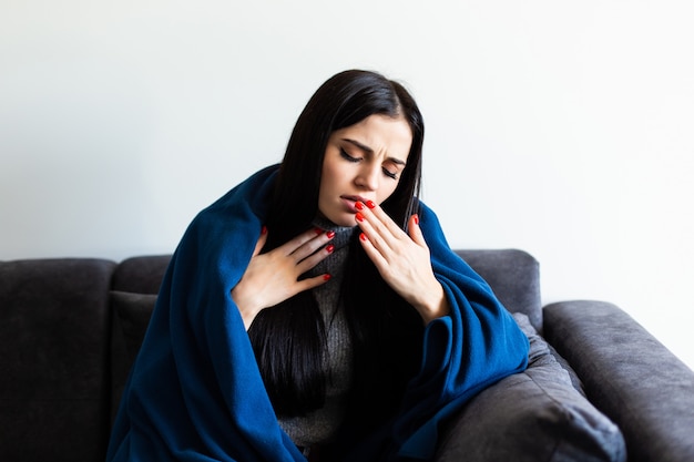 Indisposed sick woman feeling her temperature while resting on the sofa at home